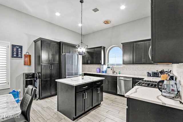 kitchen with a kitchen island, hanging light fixtures, appliances with stainless steel finishes, and light hardwood / wood-style floors