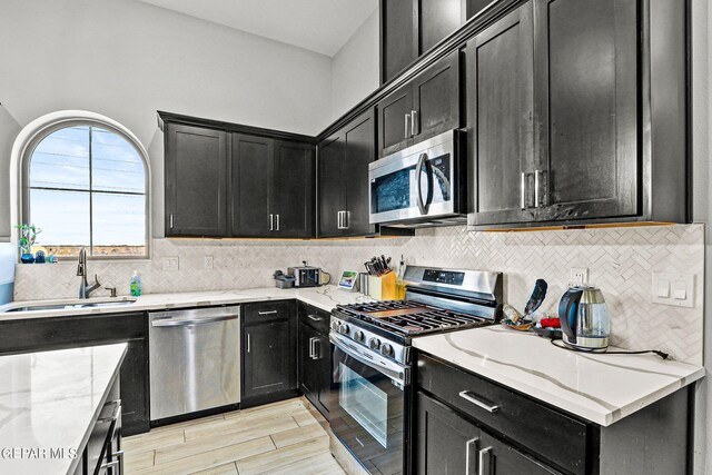 kitchen with light stone countertops, appliances with stainless steel finishes, tasteful backsplash, sink, and light wood-type flooring