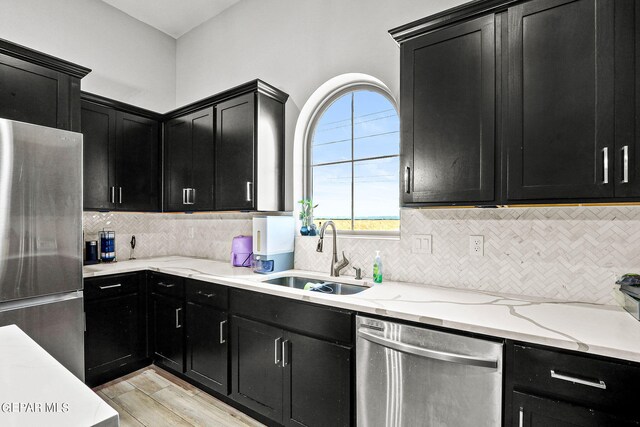 kitchen featuring appliances with stainless steel finishes, tasteful backsplash, sink, light stone counters, and light wood-type flooring