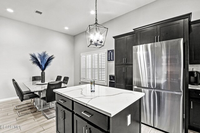 kitchen featuring an inviting chandelier, light stone countertops, a center island with sink, stainless steel refrigerator, and light wood-type flooring