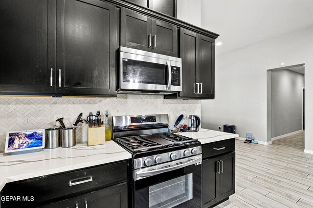 kitchen featuring appliances with stainless steel finishes, light hardwood / wood-style flooring, light stone counters, and decorative backsplash