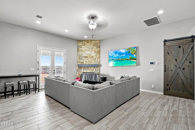 living room with a barn door, ceiling fan, french doors, and light hardwood / wood-style floors