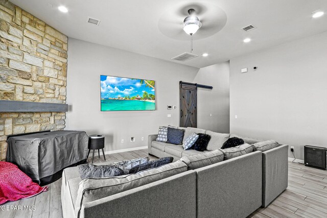 living room featuring a barn door, ceiling fan, light wood-type flooring, and a stone fireplace