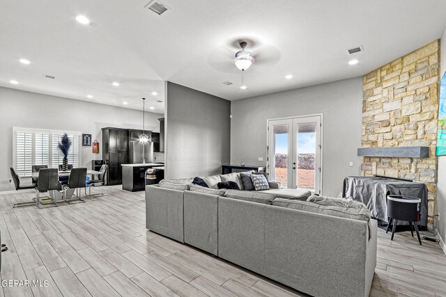 living room featuring light wood-type flooring, french doors, a fireplace, and ceiling fan