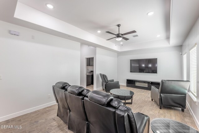 living room with a raised ceiling, ceiling fan, and light wood-type flooring