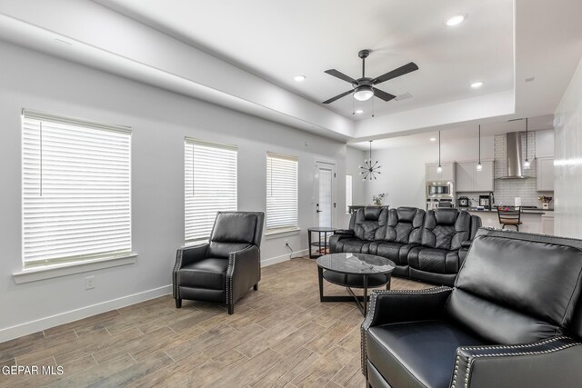 living room with a tray ceiling, wood-type flooring, and ceiling fan