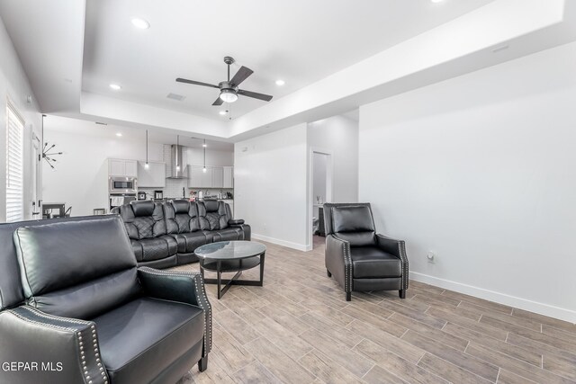 living room featuring a raised ceiling, ceiling fan, and light hardwood / wood-style floors