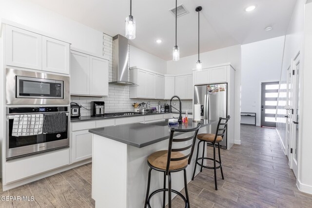 kitchen with a center island with sink, light hardwood / wood-style flooring, stainless steel appliances, and wall chimney range hood