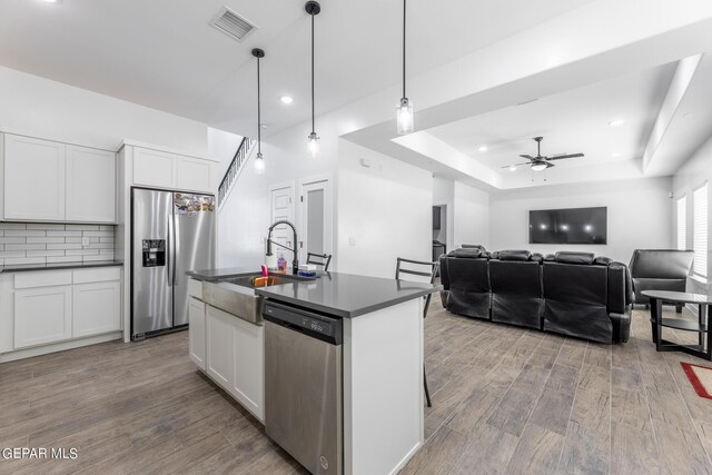 kitchen with appliances with stainless steel finishes, a kitchen island with sink, hanging light fixtures, ceiling fan, and white cabinets