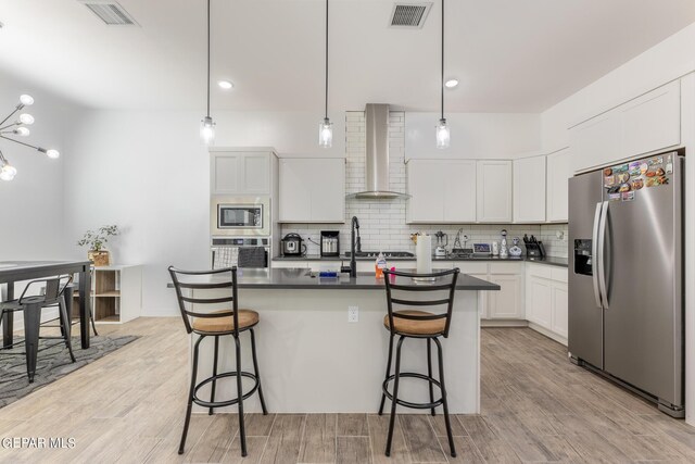 kitchen with a chandelier, light hardwood / wood-style flooring, hanging light fixtures, appliances with stainless steel finishes, and wall chimney range hood