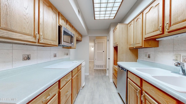 kitchen featuring decorative backsplash, appliances with stainless steel finishes, light countertops, light wood-type flooring, and a sink