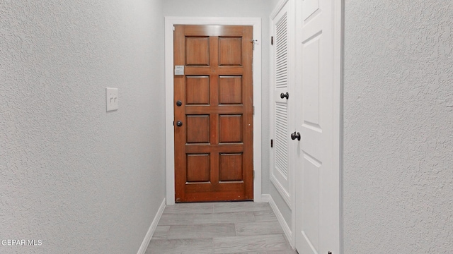 doorway to outside with a textured wall and baseboards