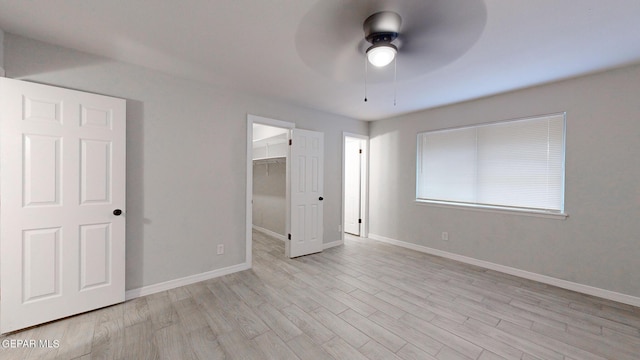 unfurnished bedroom featuring a closet, light wood-type flooring, a walk in closet, and baseboards