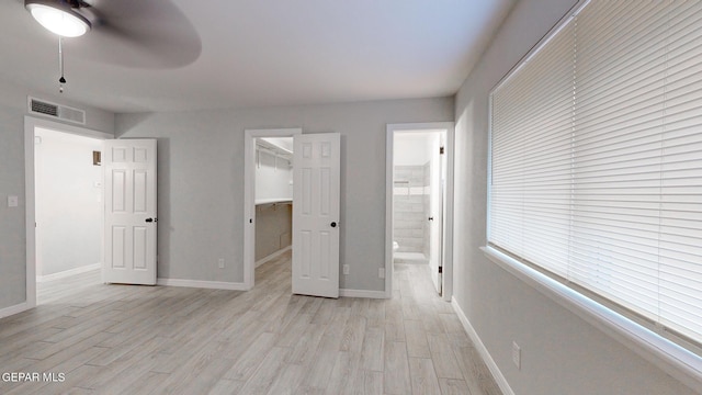 unfurnished bedroom with ensuite bathroom, light wood-style flooring, visible vents, baseboards, and a spacious closet