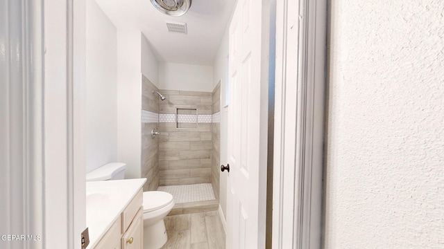 bathroom with toilet, wood finished floors, visible vents, vanity, and a stall shower