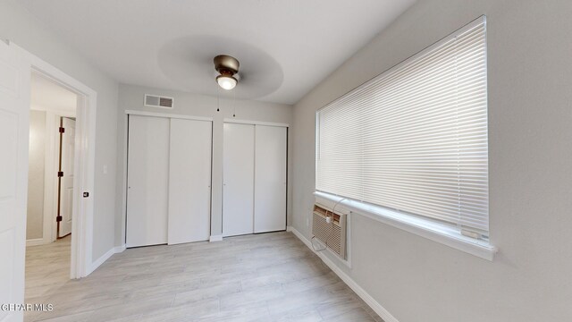 unfurnished bedroom with light wood-type flooring, ceiling fan, and multiple closets