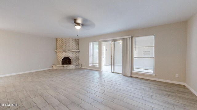 unfurnished living room with a wealth of natural light, ceiling fan, light wood-type flooring, and a brick fireplace