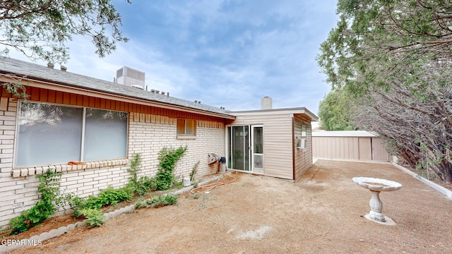 back of property featuring central AC unit, a chimney, cooling unit, a patio area, and brick siding