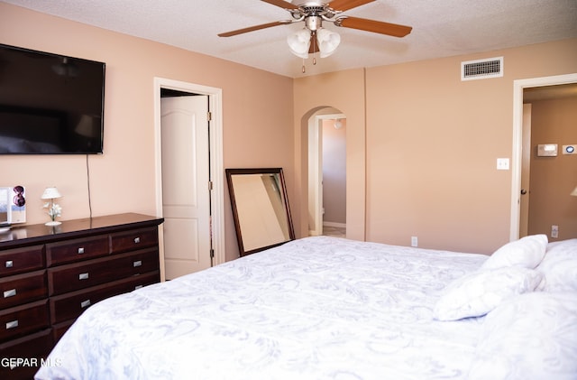 bedroom with ceiling fan, arched walkways, visible vents, and a textured ceiling