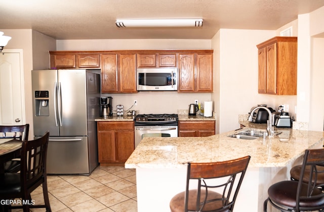 kitchen with brown cabinetry, a breakfast bar, a peninsula, a sink, and stainless steel appliances