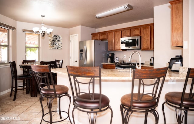 kitchen featuring appliances with stainless steel finishes, a peninsula, brown cabinetry, light tile patterned floors, and hanging light fixtures