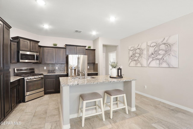 kitchen with a breakfast bar area, light stone countertops, a center island with sink, tasteful backsplash, and stainless steel appliances