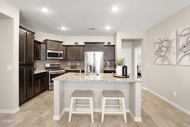 kitchen featuring light stone counters, sink, appliances with stainless steel finishes, and a kitchen island with sink