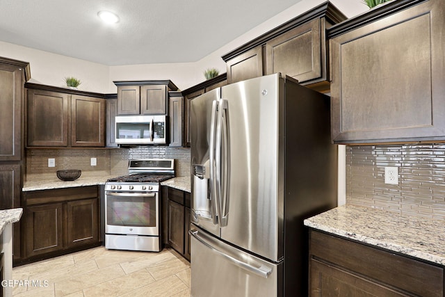 kitchen with dark brown cabinets, light stone counters, stainless steel appliances, and decorative backsplash