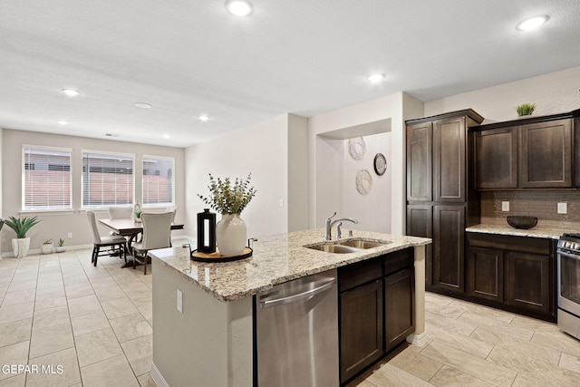 kitchen with light stone countertops, a center island with sink, tasteful backsplash, stainless steel appliances, and sink