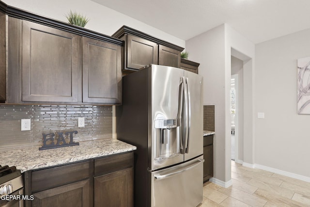 kitchen featuring stainless steel refrigerator with ice dispenser, dark brown cabinets, light stone counters, and decorative backsplash