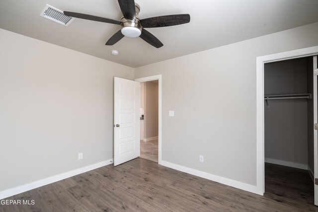 unfurnished bedroom with a closet, a spacious closet, ceiling fan, and dark wood-type flooring
