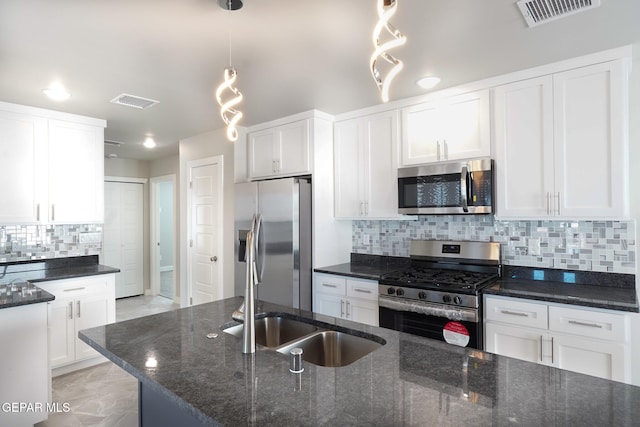 kitchen with appliances with stainless steel finishes, backsplash, dark stone counters, decorative light fixtures, and white cabinetry