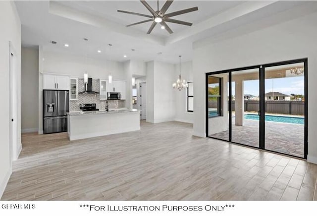 kitchen featuring ceiling fan with notable chandelier, light hardwood / wood-style floors, stainless steel appliances, white cabinetry, and wall chimney range hood