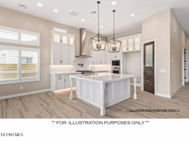 kitchen with white cabinets, built in microwave, wall chimney range hood, pendant lighting, and a center island with sink