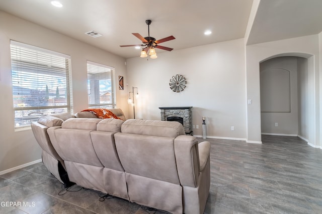 living room with arched walkways, recessed lighting, a ceiling fan, a stone fireplace, and baseboards