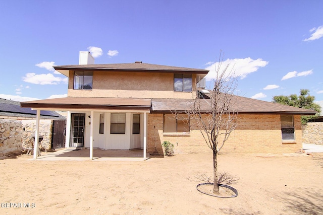 rear view of property with brick siding, a chimney, and a patio area