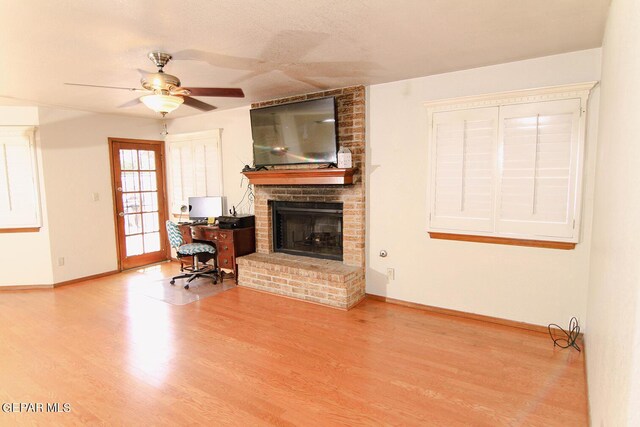 living room with a textured ceiling, a brick fireplace, hardwood / wood-style floors, and ceiling fan