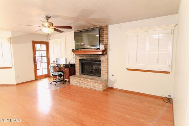 living room with a brick fireplace, ceiling fan, baseboards, and wood finished floors