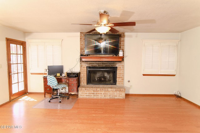 home office with a textured ceiling, wood-type flooring, a brick fireplace, and ceiling fan