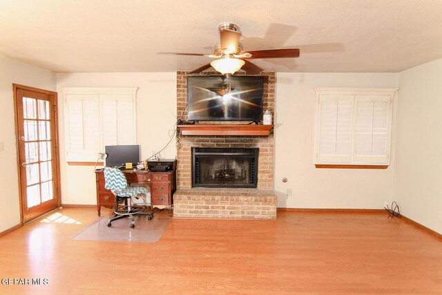 office space featuring baseboards, a ceiling fan, wood finished floors, a textured ceiling, and a brick fireplace