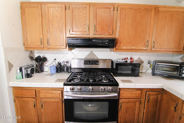 kitchen with range hood, backsplash, tile counters, and stainless steel gas range oven