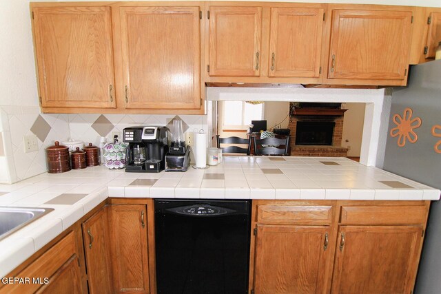 kitchen featuring a fireplace, dishwasher, backsplash, tile counters, and kitchen peninsula