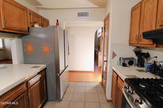 kitchen with tile countertops, light tile patterned floors, stainless steel appliances, visible vents, and backsplash