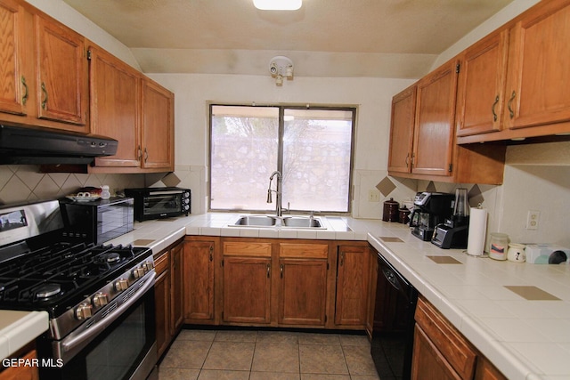 kitchen featuring tile counters, tasteful backsplash, a sink, under cabinet range hood, and black appliances