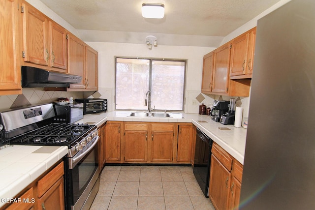 kitchen with tile countertops, a sink, under cabinet range hood, black appliances, and backsplash