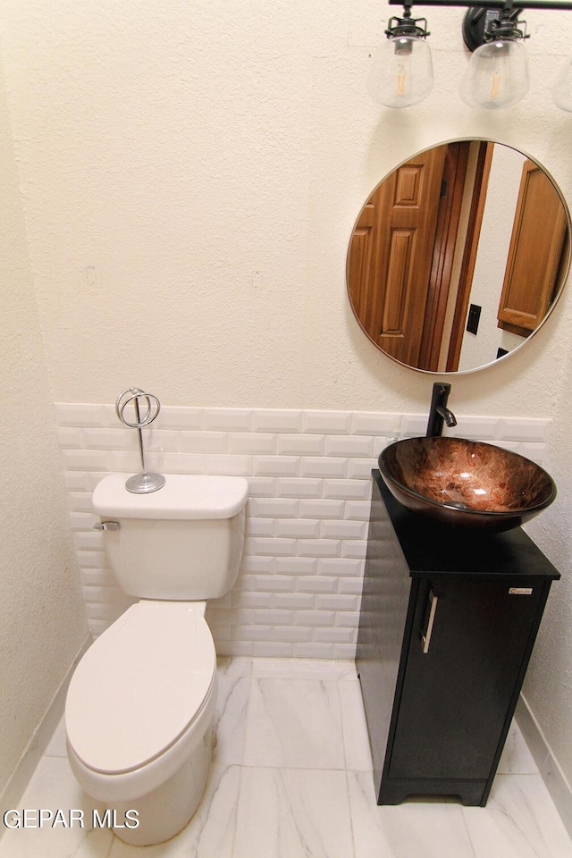 bathroom featuring marble finish floor, a textured wall, toilet, wainscoting, and vanity