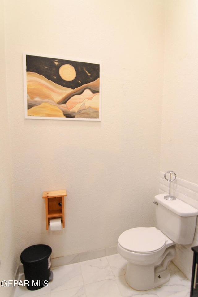 bathroom with toilet, marble finish floor, and baseboards