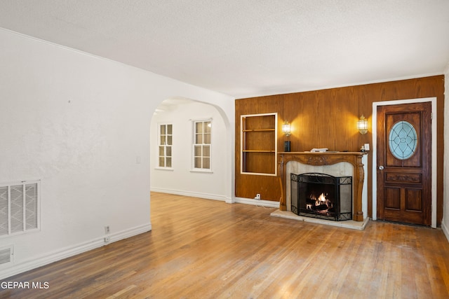 unfurnished living room with built in features, wood walls, wood-type flooring, and a textured ceiling