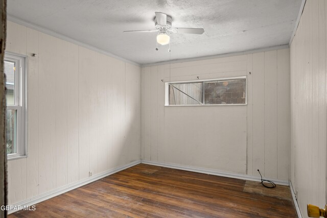 unfurnished room featuring dark wood-type flooring, wood walls, ceiling fan, and a wealth of natural light