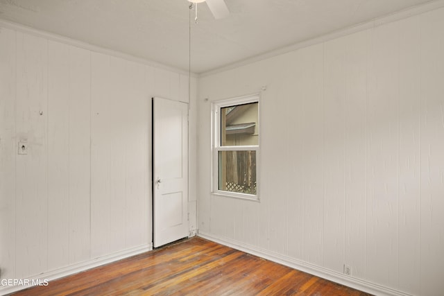 unfurnished room with ceiling fan, wooden walls, dark hardwood / wood-style flooring, and ornamental molding